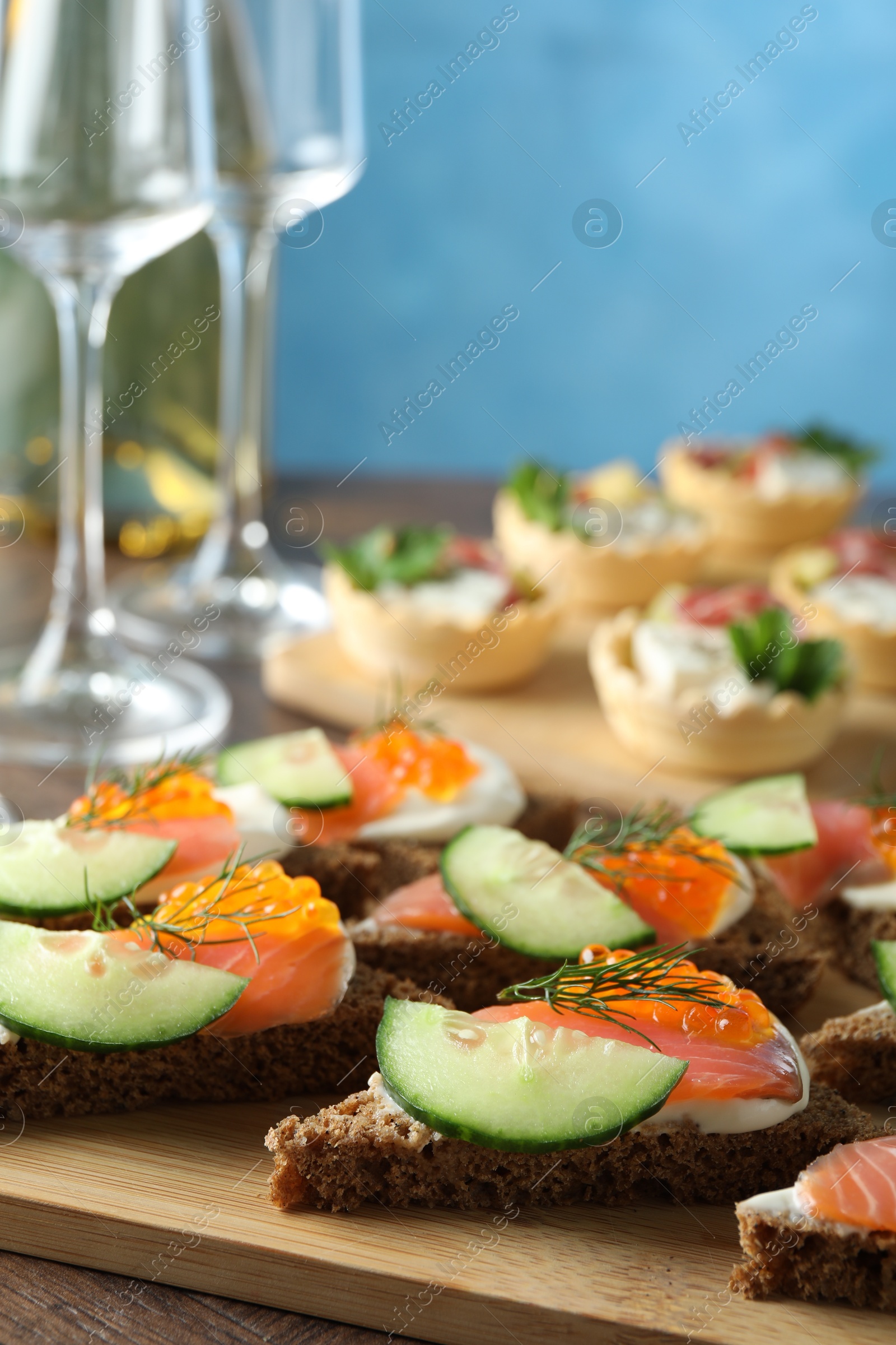 Photo of Tasty canapes with salmon and cucumber on wooden table, closeup