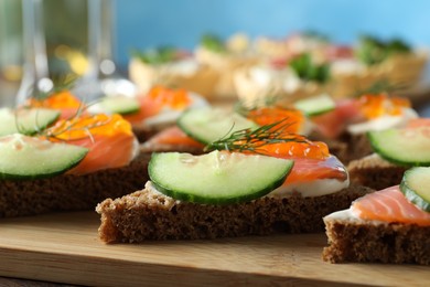 Photo of Tasty canapes with salmon and cucumber on wooden table, closeup