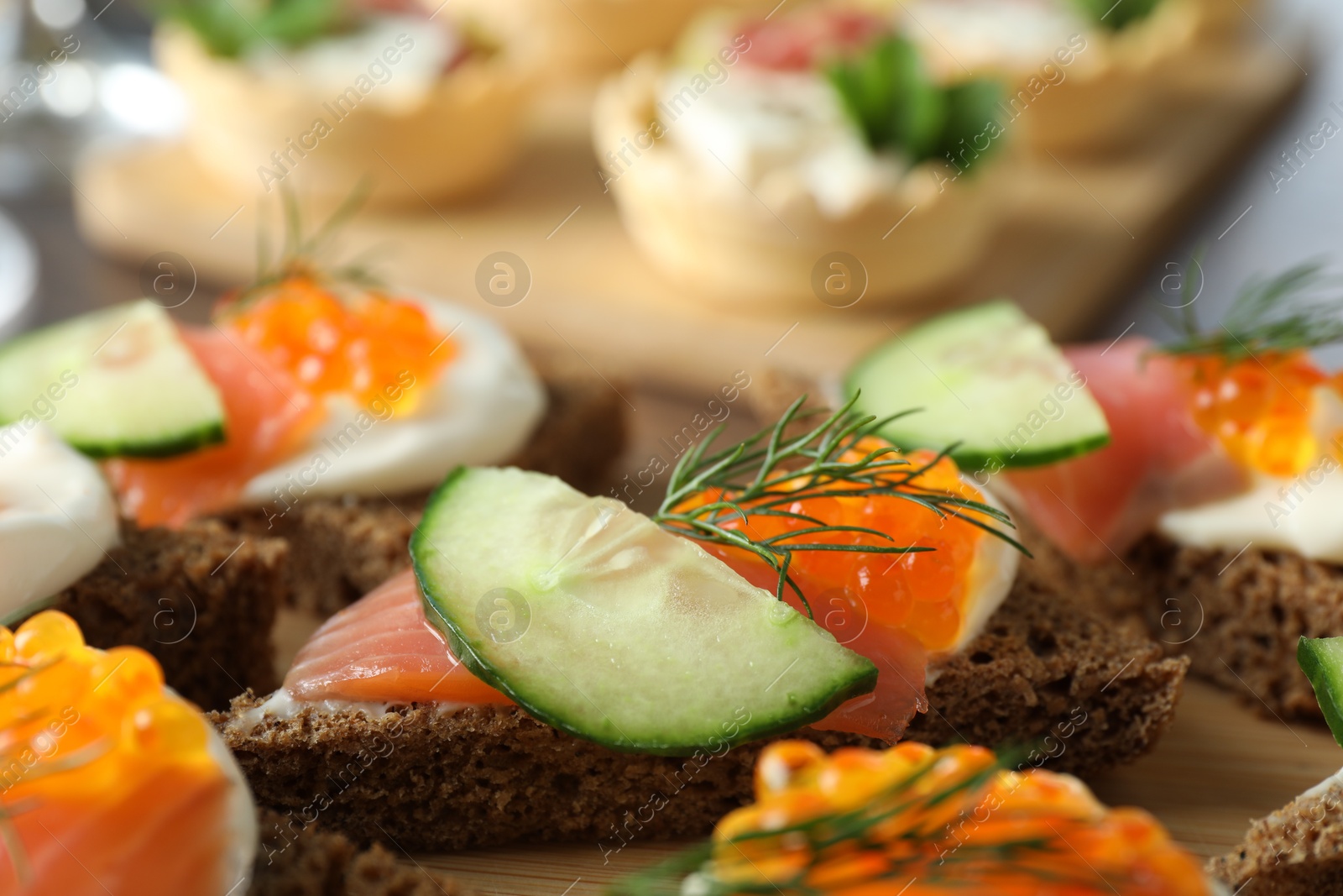 Photo of Tasty canapes with salmon and cucumber on wooden board, closeup