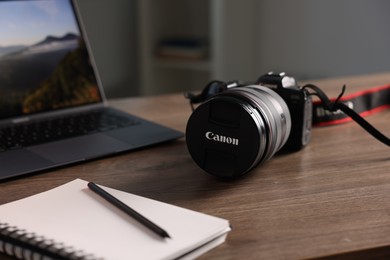 Photo of Professional photo camera, laptop and notepad on wooden desk indoors