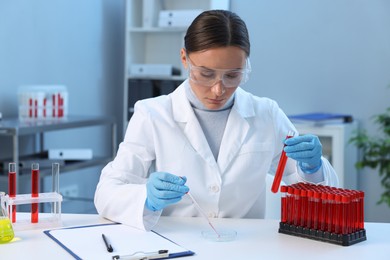 Photo of Laboratory testing. Doctor with test tube dripping blood sample into Petri dish at table indoors