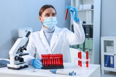 Photo of Laboratory testing. Doctor holding test tube with blood sample at table indoors