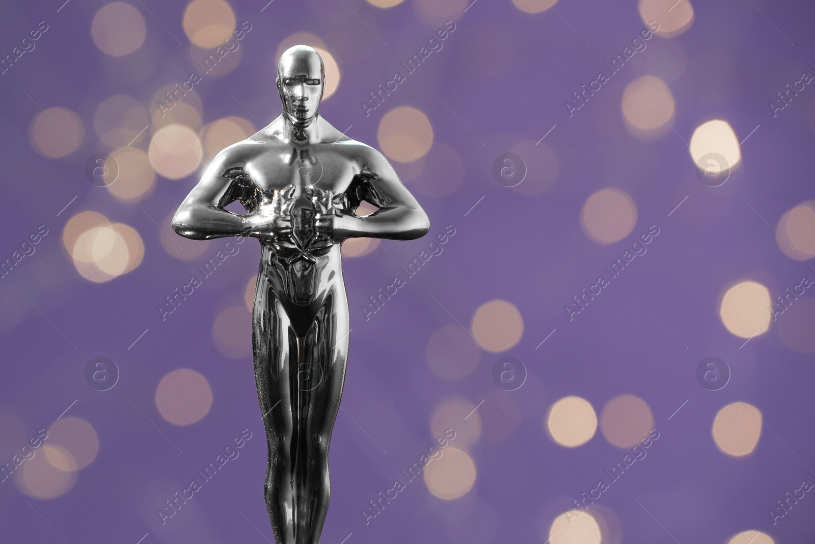 Photo of Golden trophy in shape of human figure on purple background with blurred lights, space for text