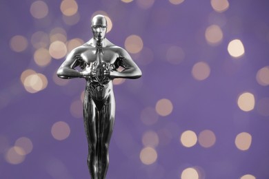 Photo of Golden trophy in shape of human figure on purple background with blurred lights, space for text