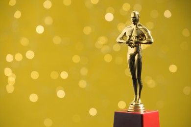 Photo of Golden trophy in shape of human figure on olive background with blurred lights, space for text