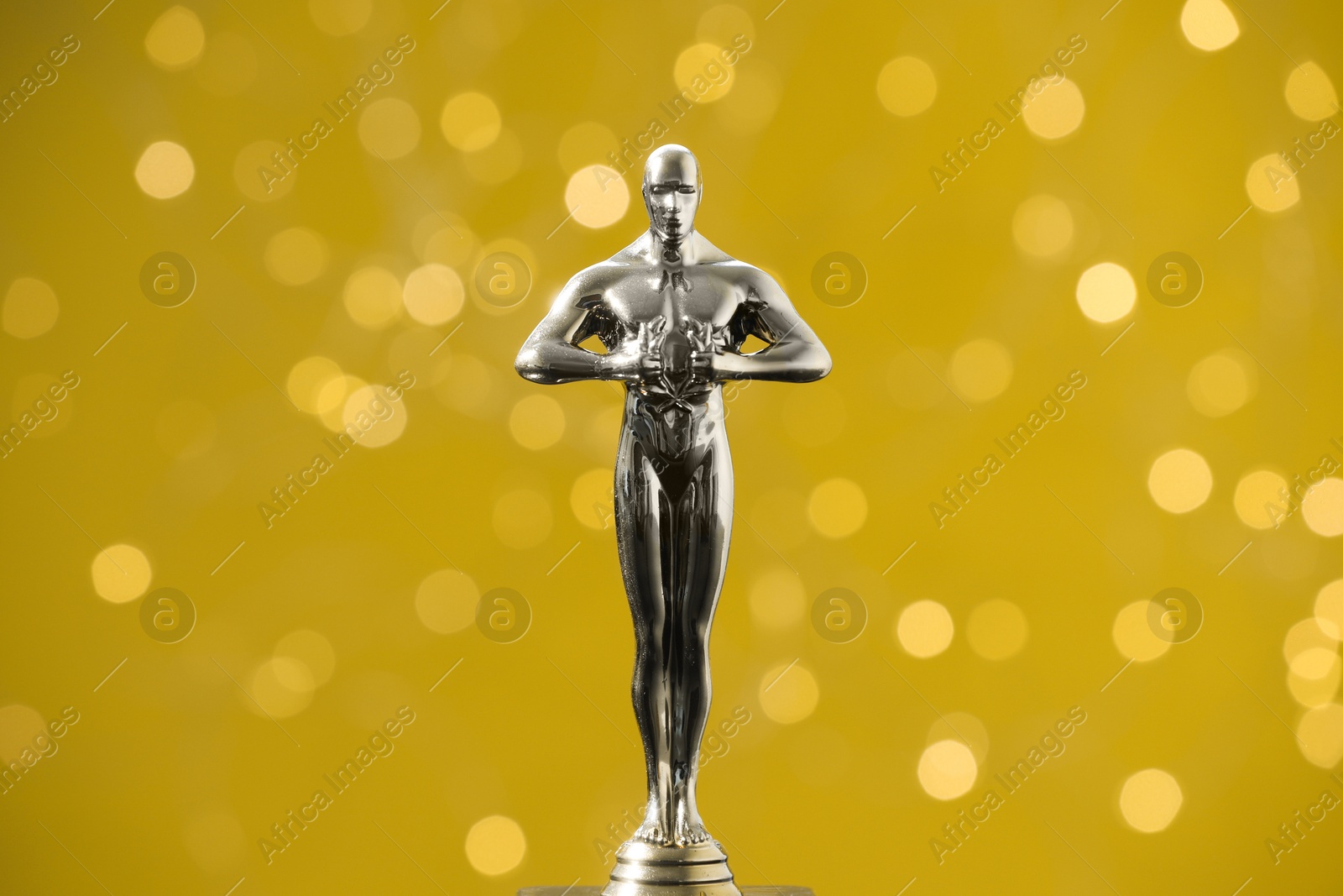 Photo of Golden trophy in shape of human figure on olive background with blurred lights