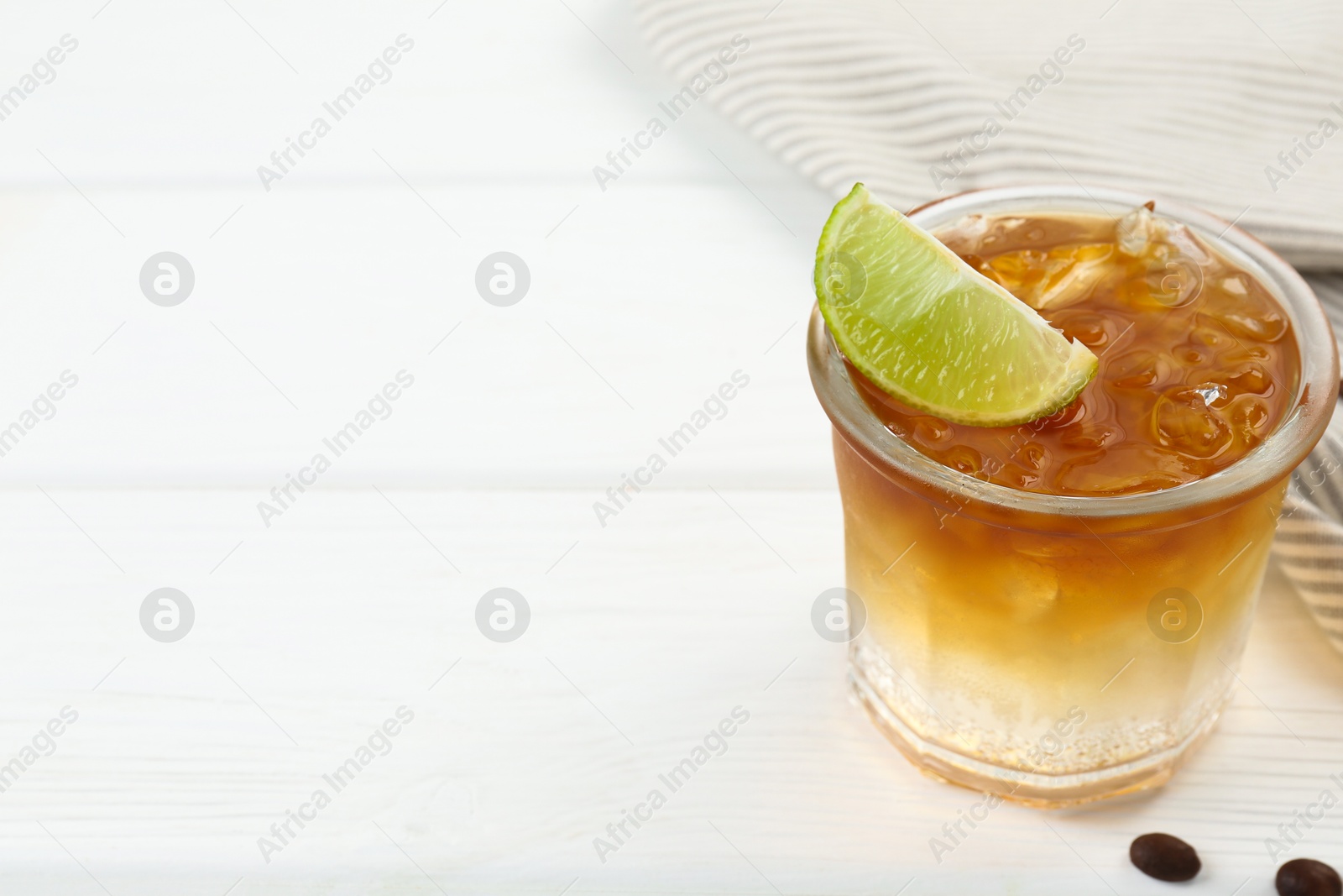 Photo of Refreshing espresso tonic drink with slice of lime and coffee beans on white wooden table, closeup. Space for text