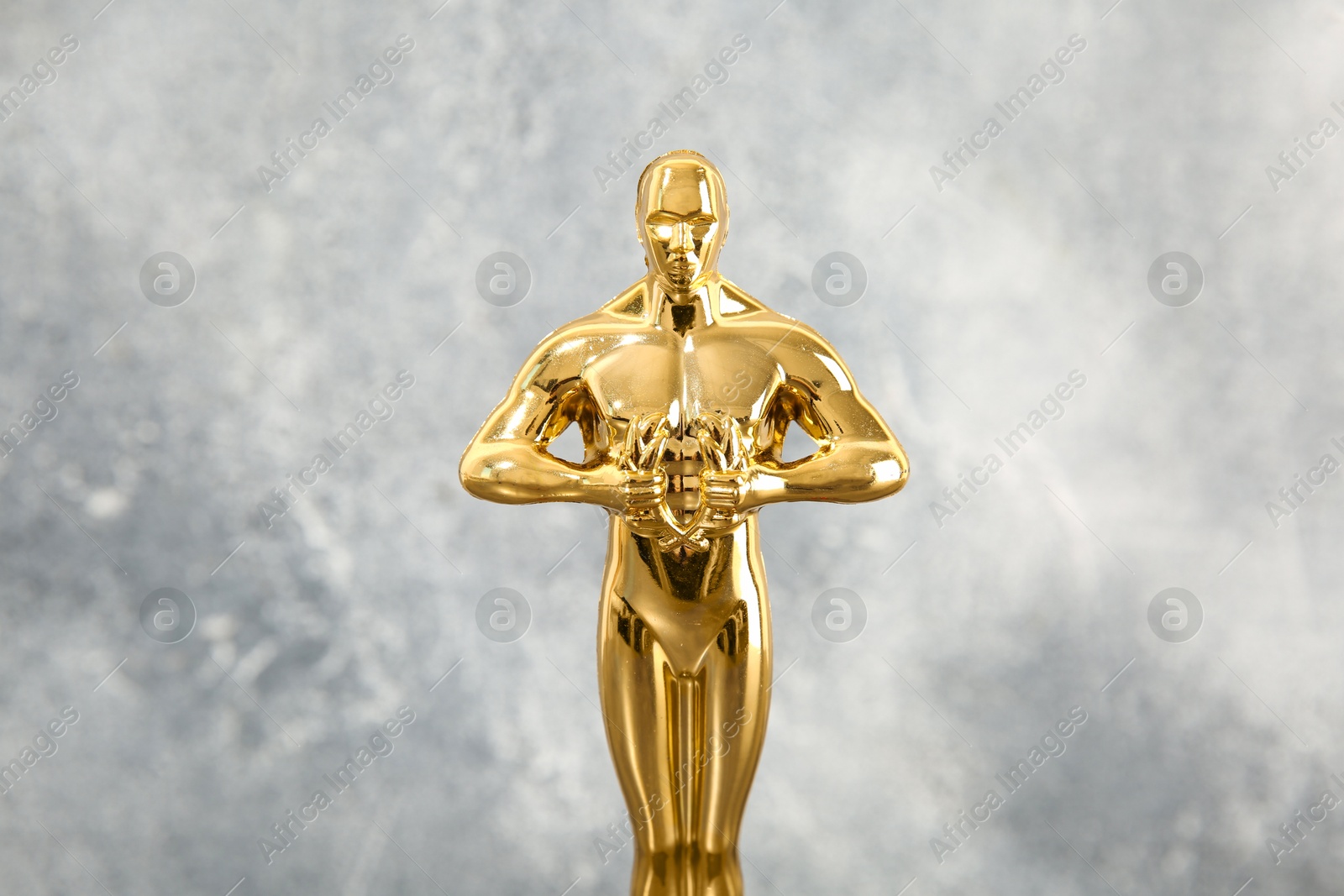 Photo of Golden trophy in shape of human figure against blurred gray background