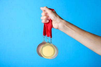 Photo of Woman with different medals on light blue background, closeup