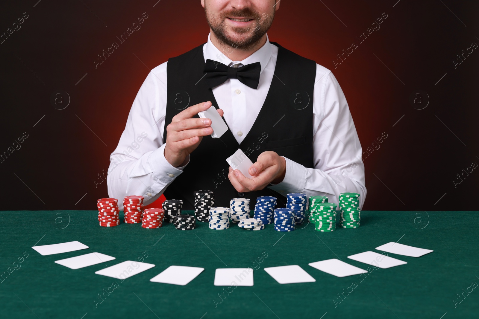 Photo of Professional croupier shuffling cards at gambling table against dark red background, closeup