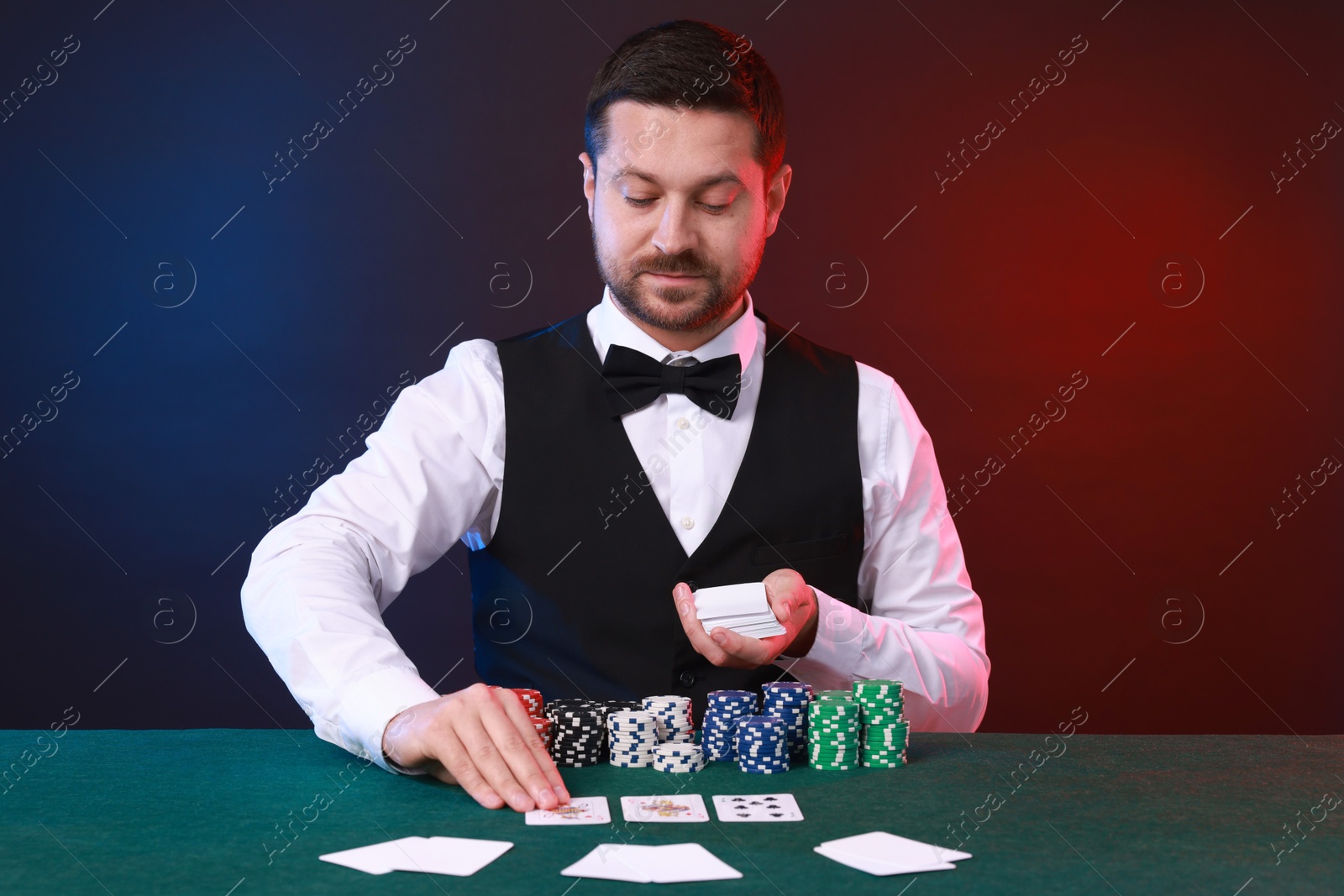 Photo of Professional croupier with playing cards at gambling table against color background