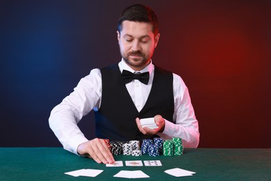 Photo of Professional croupier with playing cards at gambling table against color background