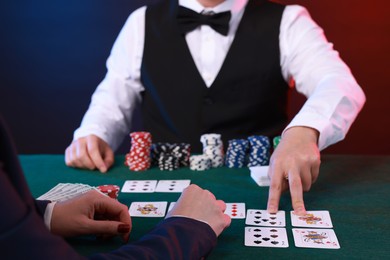 Photo of Professional croupier and gambler at table with playing cards and casino chips, closeup