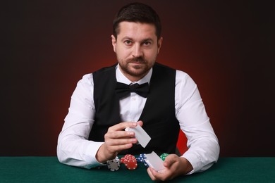 Photo of Professional croupier shuffling cards at gambling table against dark red background