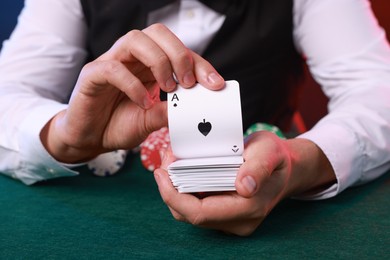 Photo of Professional croupier with playing cards at gambling table, closeup