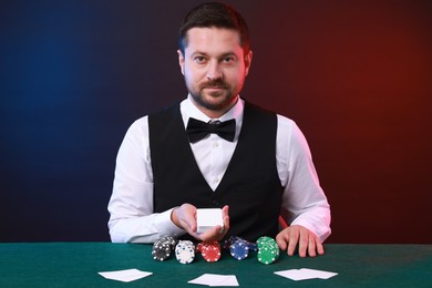 Photo of Professional croupier with playing cards at gambling table against color background