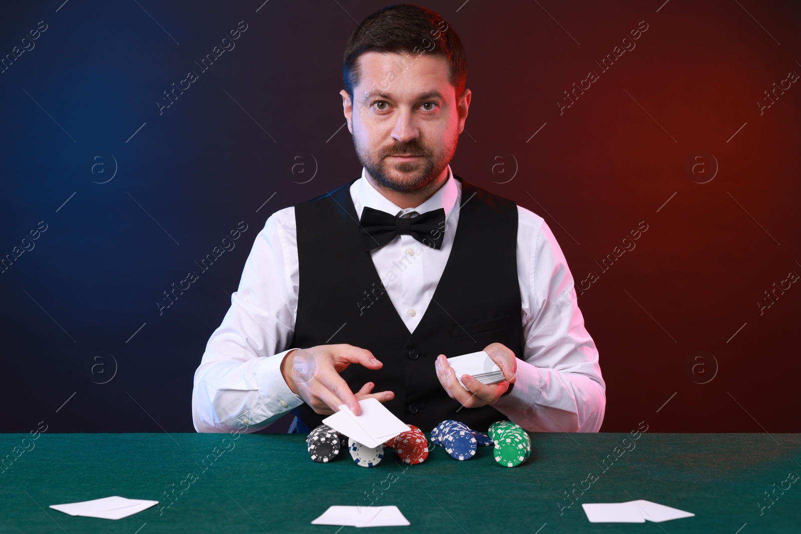 Photo of Professional croupier with playing cards at gambling table against color background