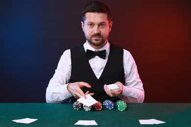 Photo of Professional croupier with playing cards at gambling table against color background