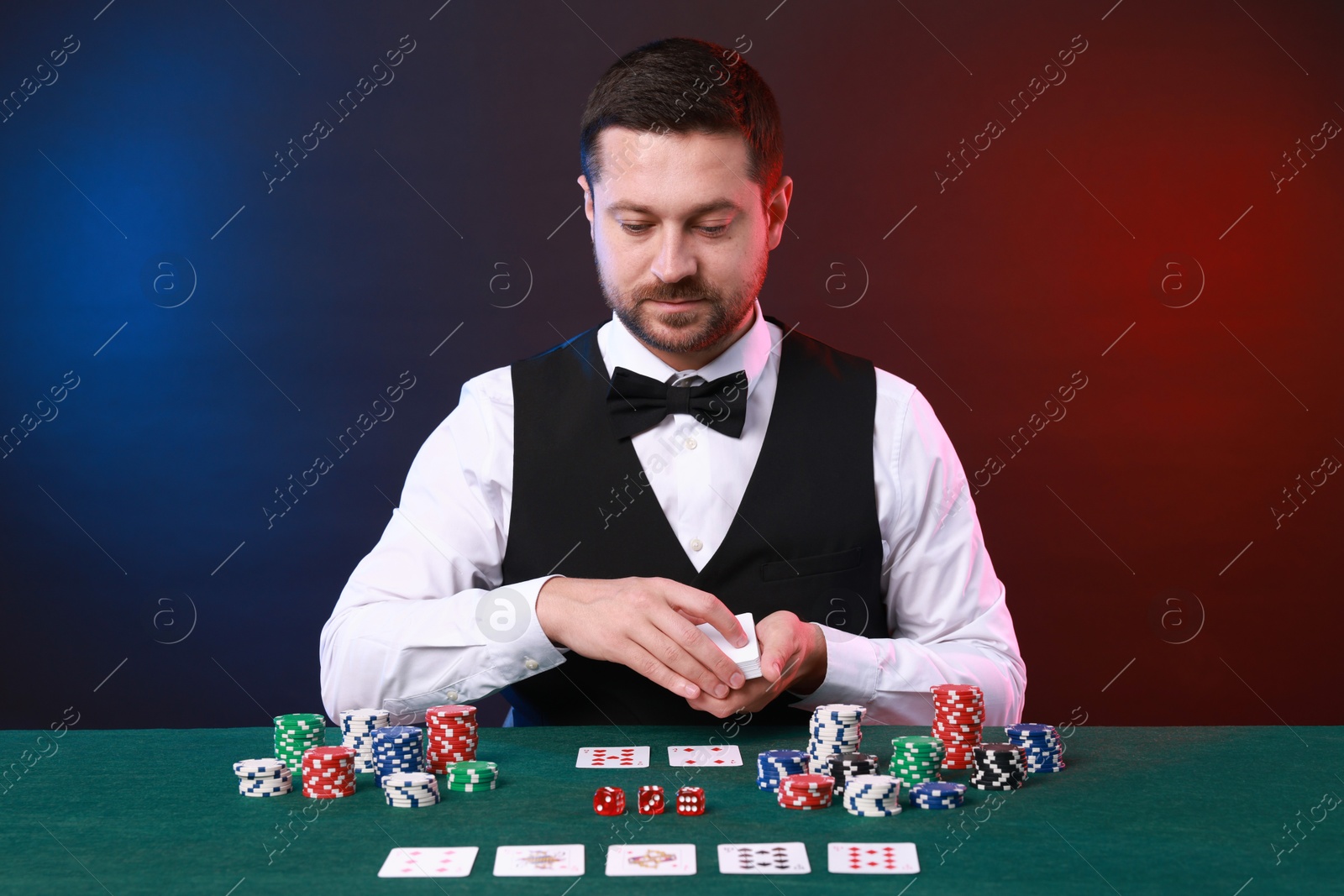 Photo of Professional croupier with playing cards at gambling table against color background