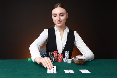 Professional croupier with casino chips and playing cards at gambling table on color background