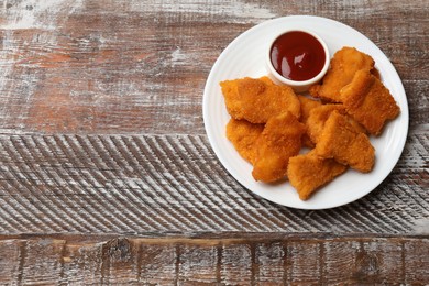 Photo of Delicious chicken nuggets with ketchup on wooden table, top view. Space for text