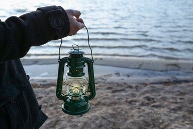 Photo of Man with vintage kerosene lamp on beach in evening, closeup