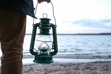 Photo of Man with vintage kerosene lamp on beach in evening, closeup