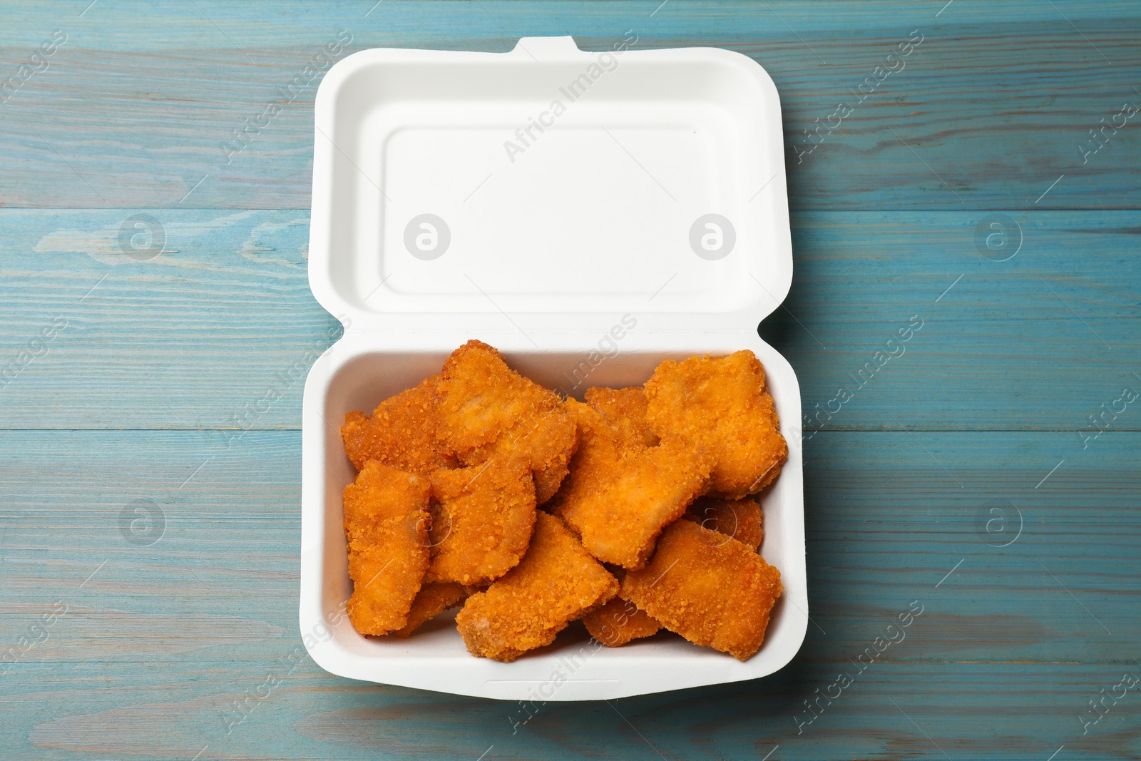 Photo of Delicious chicken nuggets in takeaway container on blue wooden table, top view