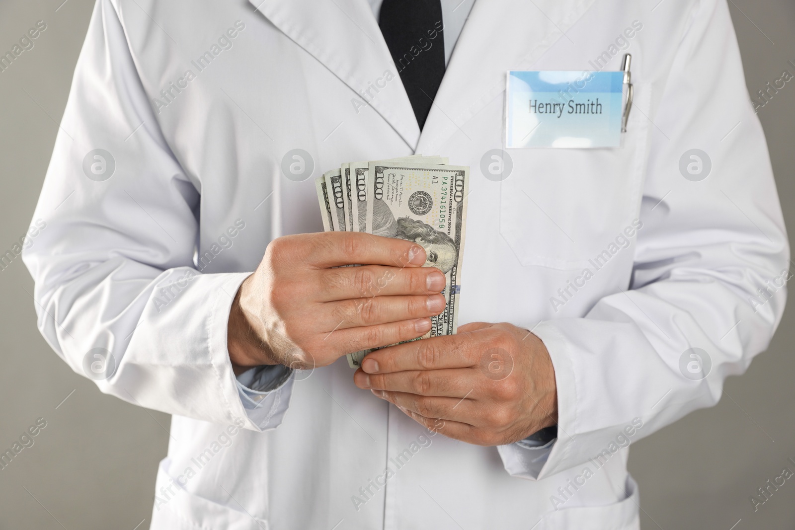 Photo of Corruption concept. Doctor with dollar banknotes on grey background, closeup