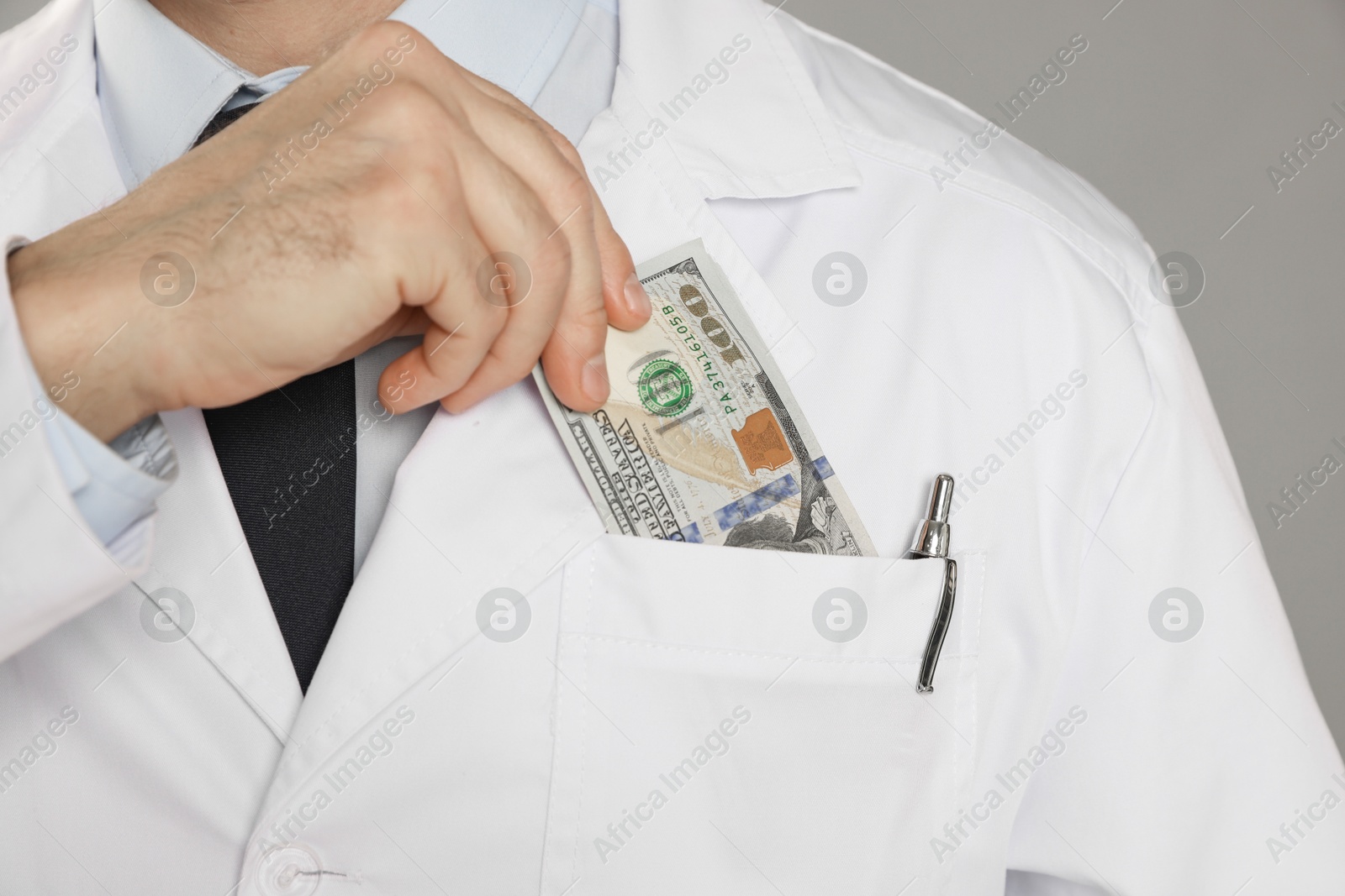 Photo of Corruption concept. Doctor putting dollar banknotes into his pocket on grey background, closeup