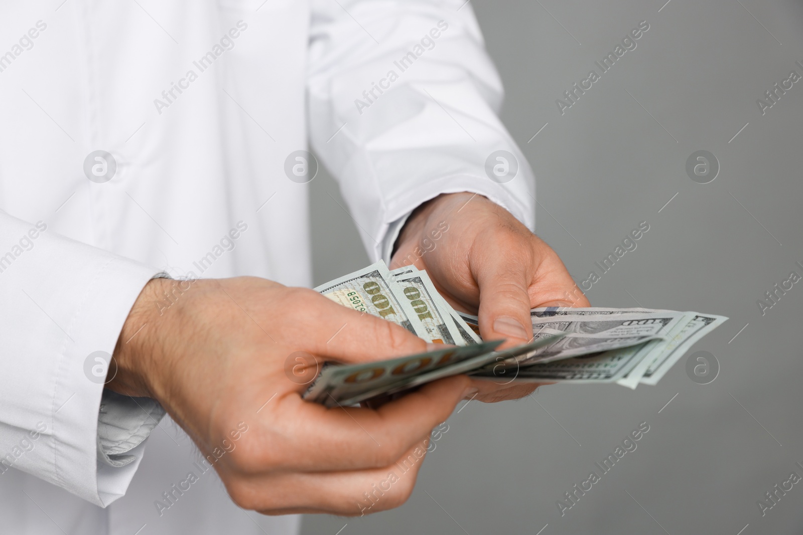 Photo of Corruption concept. Doctor with dollar banknotes on grey background, closeup