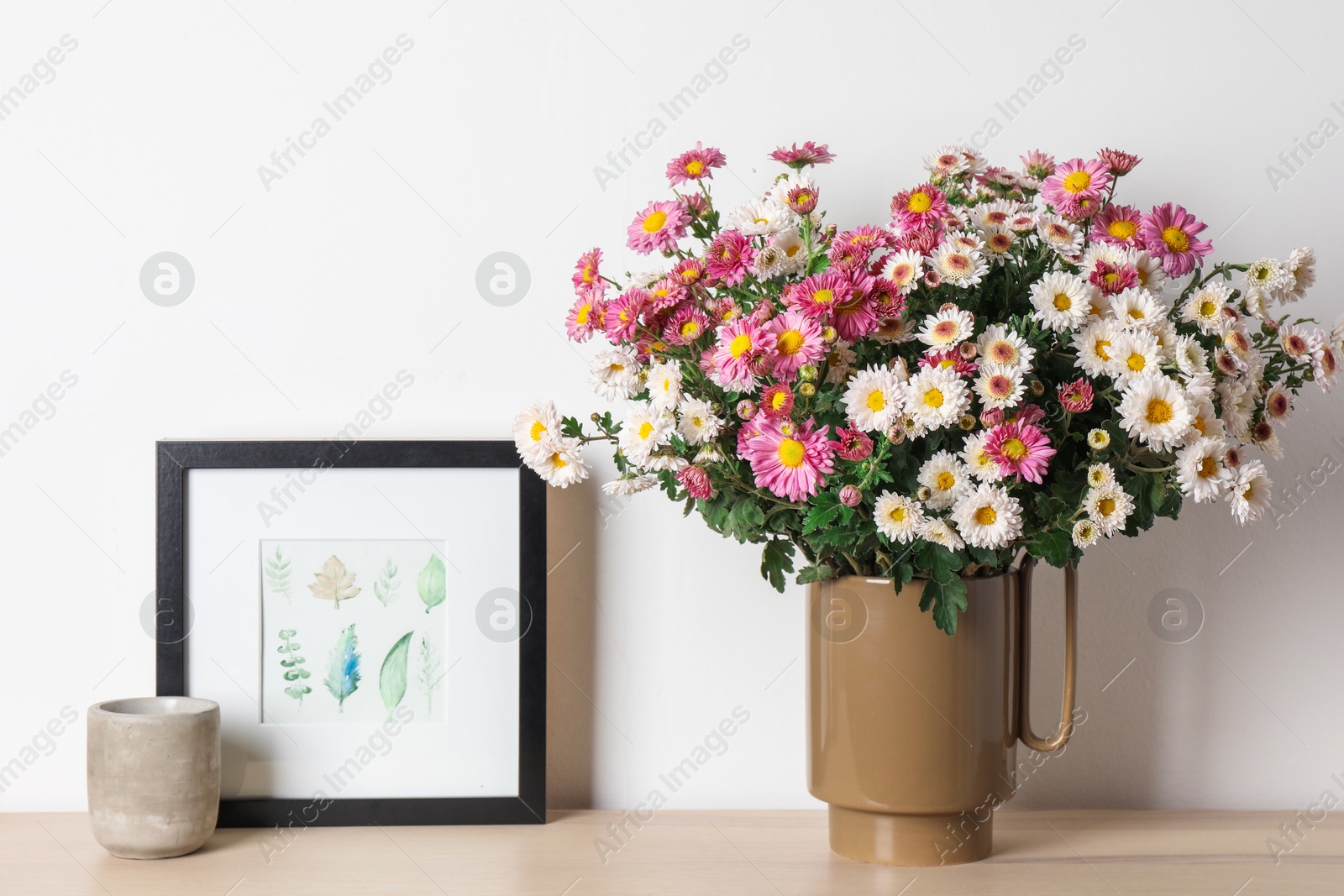 Photo of Vase with beautiful flowers and other decor on wooden shelf near white wall