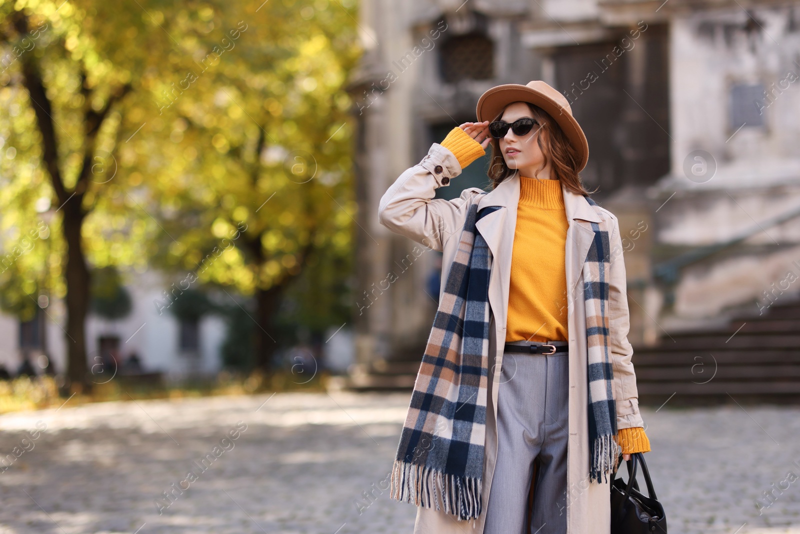 Photo of Charming young woman in stylish outfit on city street, space for text. Autumn season