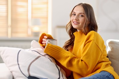 Photo of Charming young woman with cup of hot drink on sofa at home. Autumn atmosphere