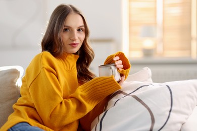 Photo of Charming young woman with cup of hot drink on sofa at home. Autumn atmosphere