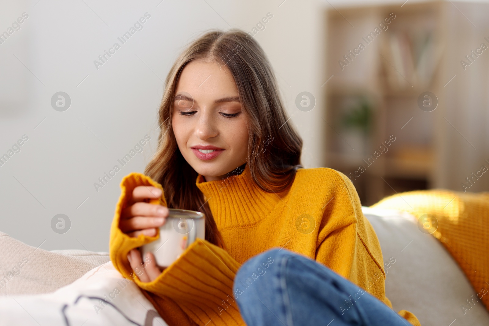 Photo of Charming young woman with cup of hot drink on sofa at home. Autumn atmosphere