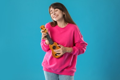 Happy woman playing ukulele on light blue background