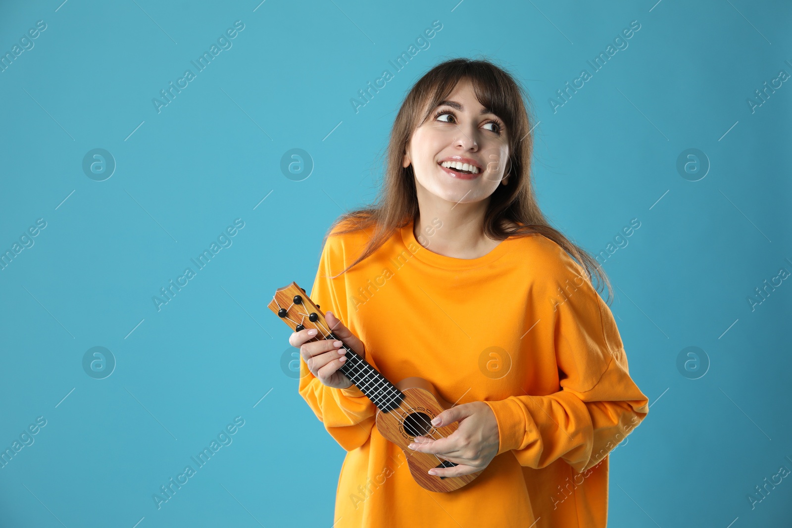 Photo of Happy woman playing ukulele on light blue background