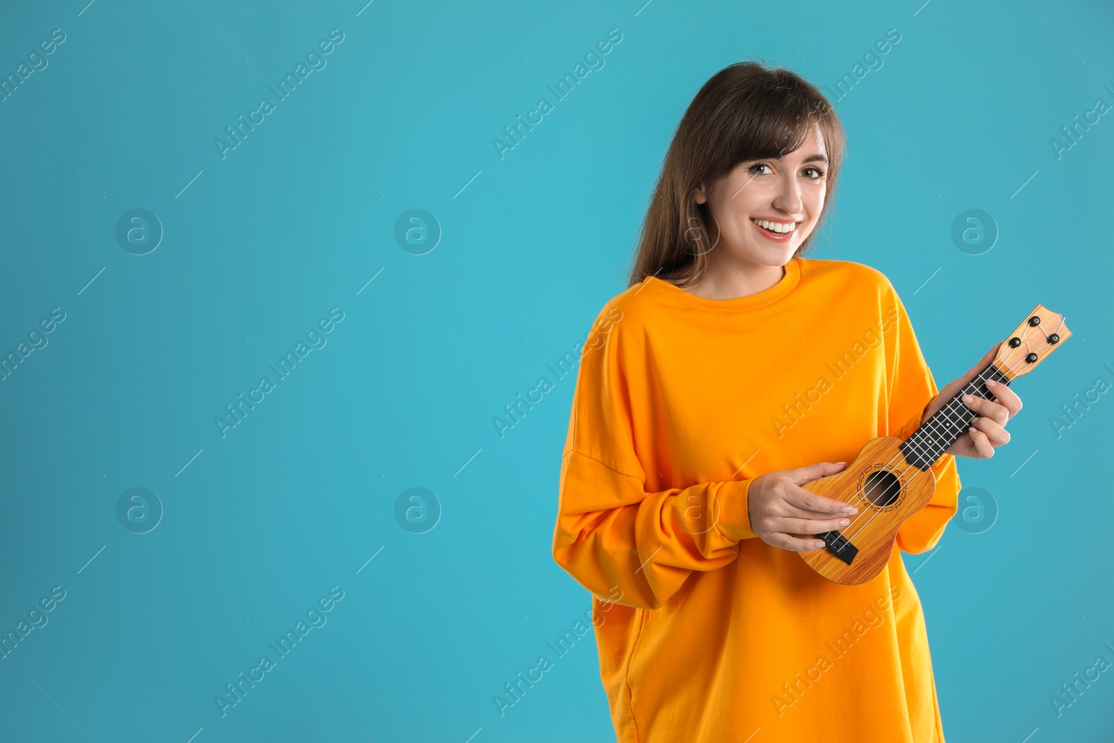 Photo of Happy woman playing ukulele on light blue background, space for text