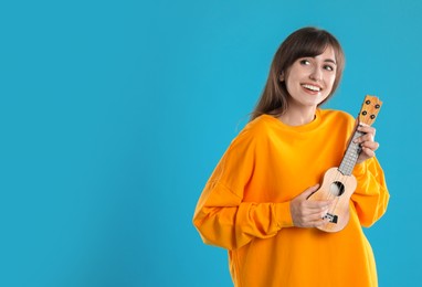 Photo of Happy woman playing ukulele on light blue background, space for text