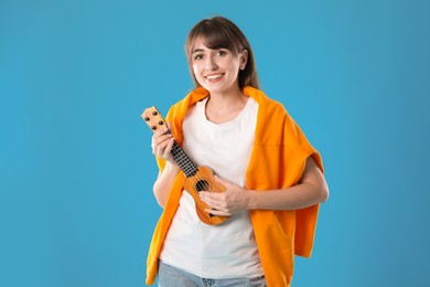 Photo of Happy woman playing ukulele on light blue background