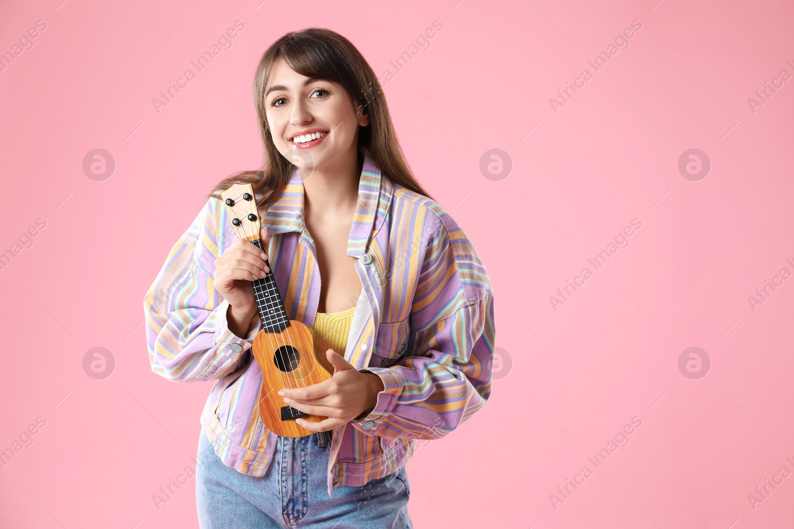 Photo of Happy woman playing ukulele on pink background, space for text