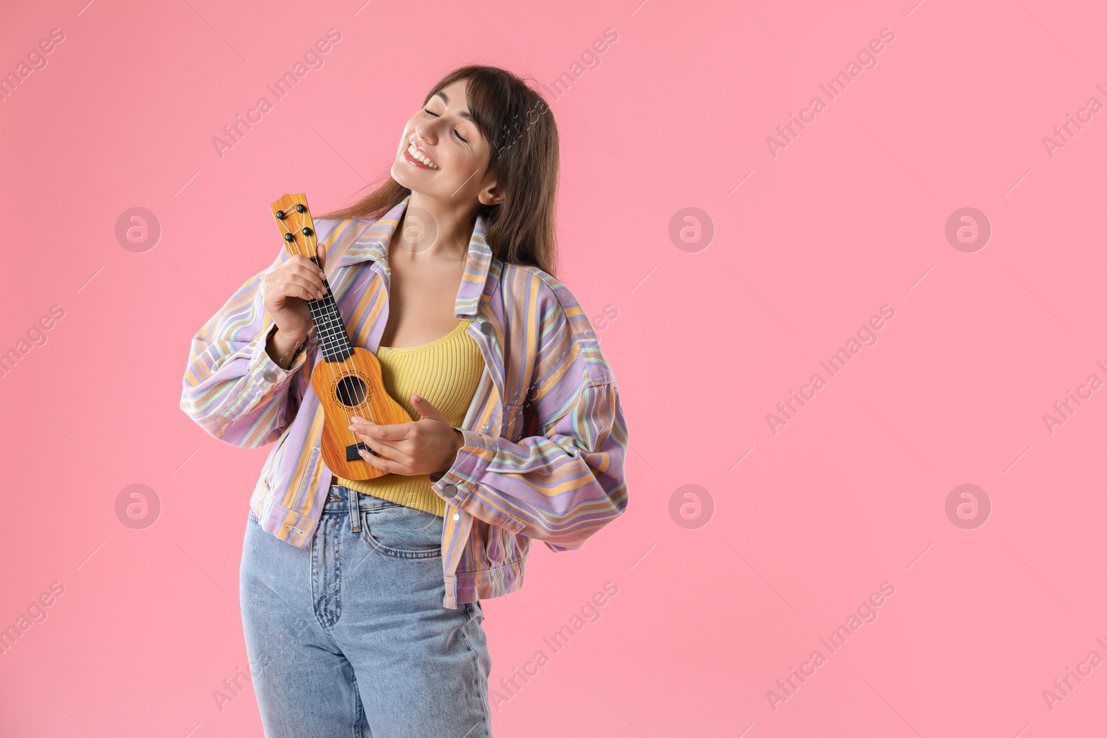 Photo of Happy woman playing ukulele on pink background, space for text