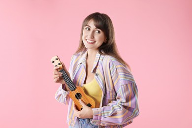 Happy woman playing ukulele on pink background