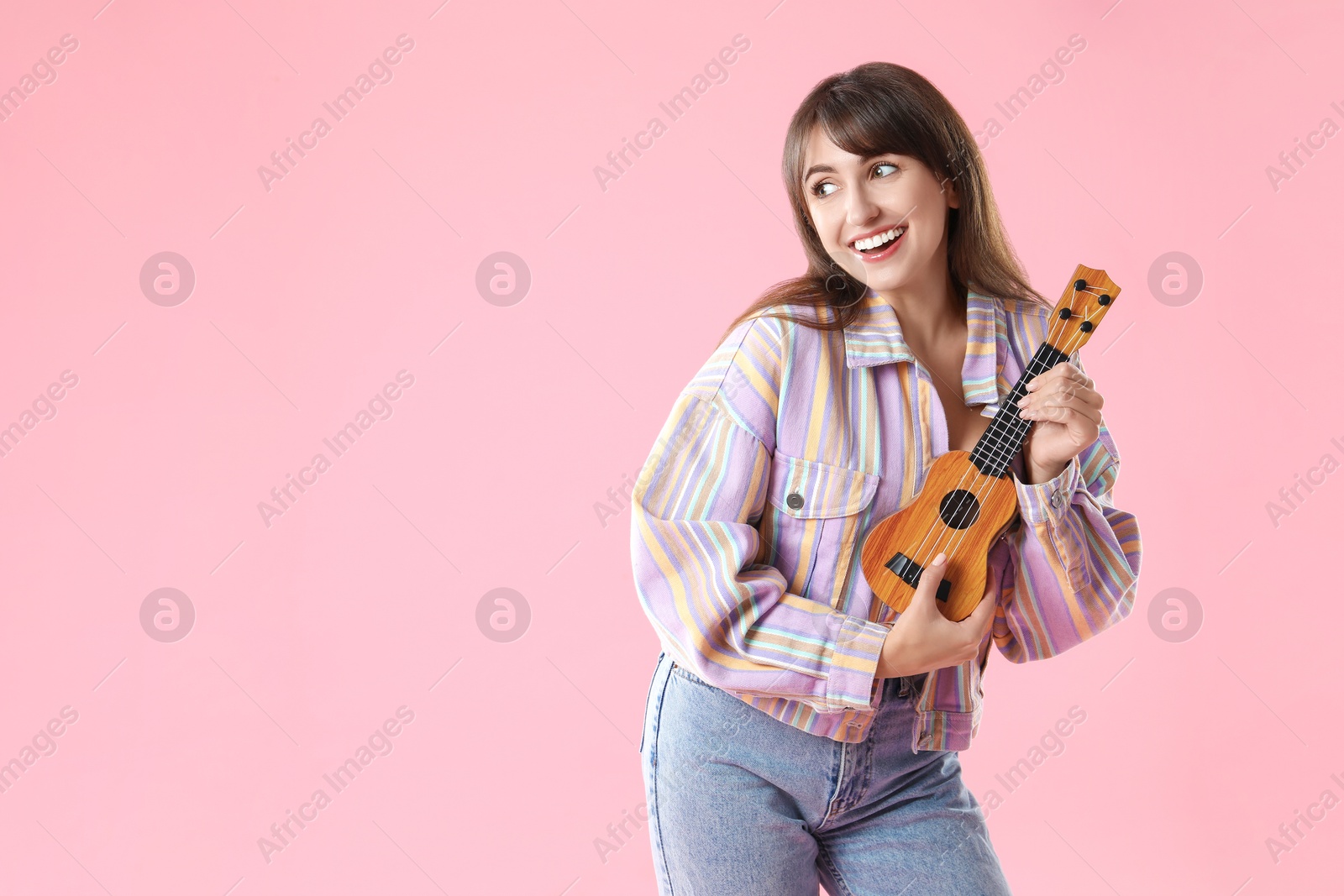 Photo of Happy woman playing ukulele on pink background, space for text