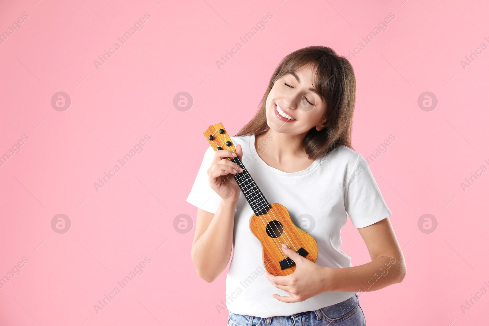 Photo of Happy woman playing ukulele on pink background, space for text