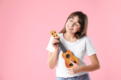 Photo of Happy woman playing ukulele on pink background, space for text