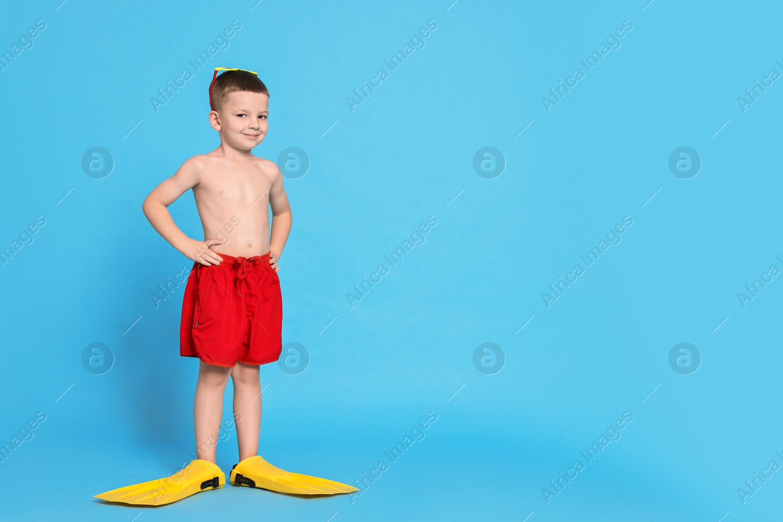 Photo of Cute little boy in beachwear and fins on light blue background. Space for text