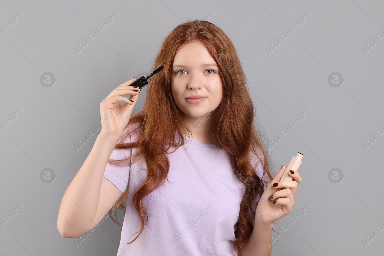 Photo of Teenage girl applying mascara on light grey background