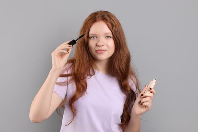 Teenage girl applying mascara on light grey background